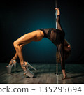 Pole dancer arching back on pole under dramatic studio lighting, high heels and sheer costume highlighting toned muscles and graceful curve, expressive silhouette conveying strength and sensual 135295694