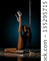 Seated pole dance pose with raised leg and glitter heels, elongated line and elegant hand placement framing editorial glamour vibe, soft rim lighting highlighting skin tone and poised expression 135295715