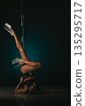 Floor inversion with legs extended upward gripping pole, heels sparkling against moody backdrop, core strength and focused expression conveying disciplined training and pole dance performance energy 135295717