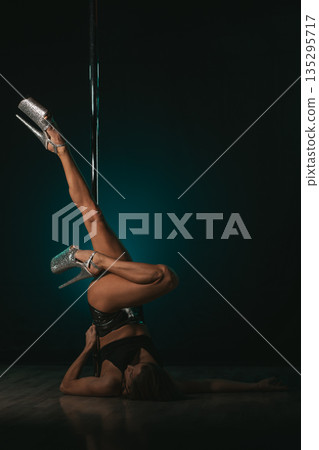 Floor inversion with legs extended upward gripping pole, heels sparkling against moody backdrop, core strength and focused expression conveying disciplined training and pole dance performance energy Floor inversion with legs extended upward gripping pole, heels sparkling against moody backdrop, core strength and focused expression conveying disciplined training and pole dance performance energy 135295717