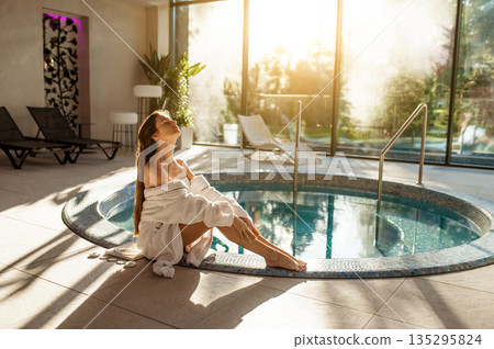 Cute young woman in white bathrobe spending her time at spa center Cute young woman in white bathrobe spending her time at spa center 135295824