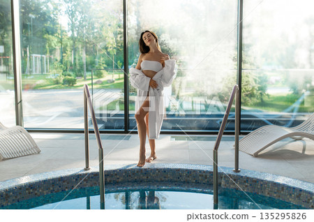 Cute young woman in white bathrobe spending her time at spa center Cute young woman in white bathrobe spending her time at spa center 135295826