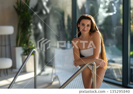 Pretty long-haired woman standing near the pool in spa salon and looking relaxed 135295840
