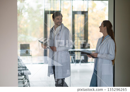 Female doctor standing near the flipchart and presenting something to a new doctor Female doctor standing near the flipchart and presenting something to a new doctor 135296265