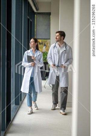 Doctors walking in the clinic corridor and discussing investigation results 135296268