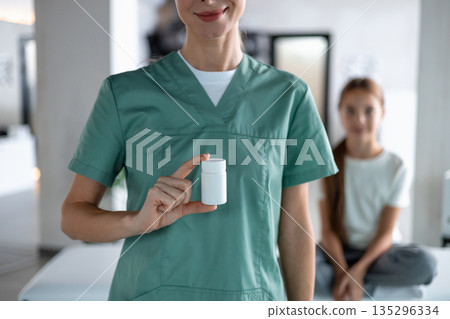 Nurse holding pill bottle in clinic with child patient 135296334
