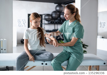 Woman therapist rubbing cream on little girl arm before massaging Woman therapist rubbing cream on little girl arm before massaging 135296336