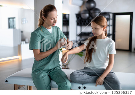 Woman therapist applying cream to little girl arm 135296337