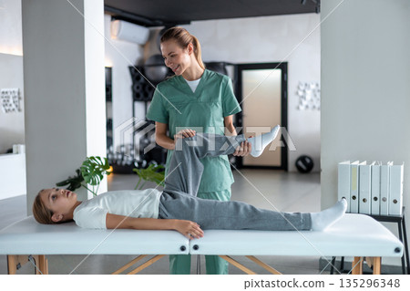 Woman therapist examining little girl leg lying on couch 135296348