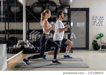 Young man and woman exercising with dumbbells and doing forward lunge 135296643