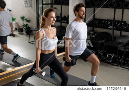Young man and woman exercising with dumbbells and doing forward lunge 135296646