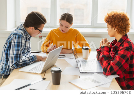 Teamwork brainstorm. Diverse colleagues working together discuss financial statistics. Group of happy young modern people sitting in creative office discussing business. Young professional team 135296768