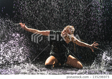 Contemporary woman dancer posing in rain water on black background. Female artist performer dancing with expression. Modern ballerina dancing in darkness. Passion dance in dark. Flexibility balance 135296973