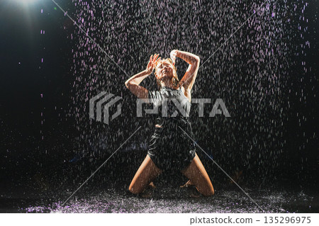 Contemporary woman dancer posing in rain water on black background. Female artist performer dancing with expression. Modern ballerina dancing in darkness. Passion dance in dark. Flexibility balance 135296975