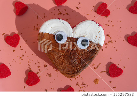 Creative flat lay with funny joke eyes on Delicious fresh croissant topped with colorful flavor Ganache. Creation unique heart shape bakery. Puff pastry holiday love gift present idea Valentine's day 135297588