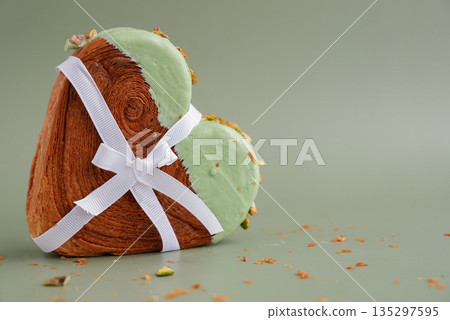 Gift present idea for love Valentine's Day holiday celebration Heart shaped pistachio croissant on green background with copy space. Puff pastry trendy sweet dessert bakery. Creamy dough experiment  135297595