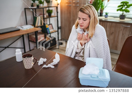 Feeling under the weather while wrapped in a cozy blanket at home Feeling under the weather while wrapped in a cozy blanket at home 135297888