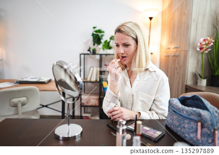Woman applying lipstick at a stylish vanity in a modern room 135297889