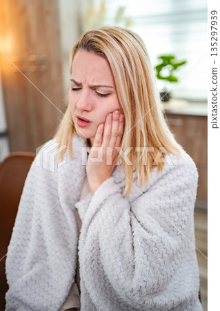 Woman experiencing dental pain while wrapped in a cozy blanket at home Woman experiencing dental pain while wrapped in a cozy blanket at home 135297939