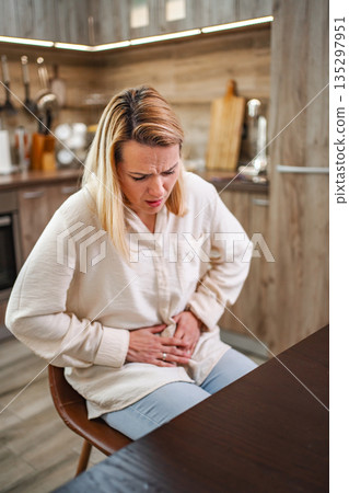 Woman in a kitchen experiencing discomfort and pain during mealtime Woman in a kitchen experiencing discomfort and pain during mealtime 135297951