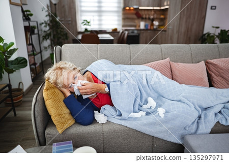 Cozy woman rests on couch with tissues in a warm living room Cozy woman rests on couch with tissues in a warm living room 135297971