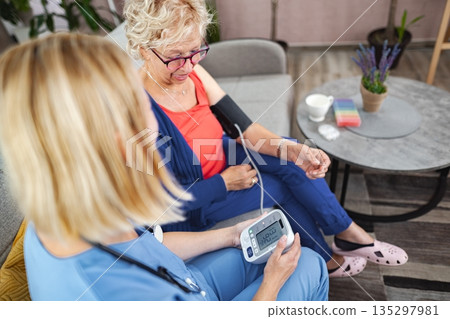 Health check-up session with a caregiver and a senior woman in a cozy setting 135297981