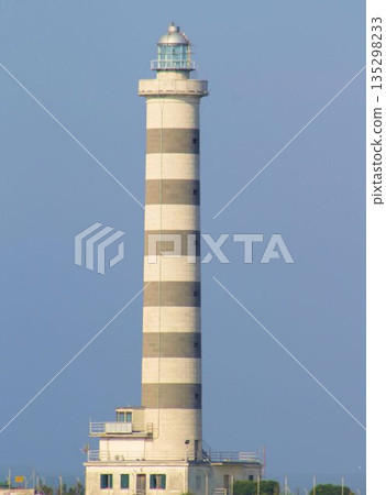 The iconic lighthouse of Lido di Jesolo situated at the mouth of the Sile river. Coastal landscape with the lighthouse tower against a clear sky, a famous landmark of the Venetian Riviera, Italy. The iconic lighthouse of Lido di Jesolo situated at the mouth of the Sile river. Coastal landscape with the lighthouse tower against a clear sky, a famous landmark of the Venetian Riviera, Italy. 135298233