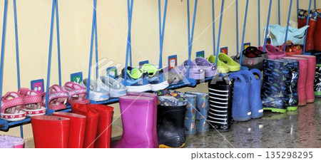 Rows of children's shoes and boots in a preschool hallway 135298295