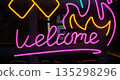 A glowing neon light sign mounted on a dark window, featuring the word Welcome in bright pink cursive typography 135298296