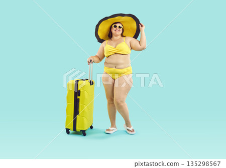 Fat woman in sunglasses wearing beach hat and swimsuit with suitcase on studio blue background. 135298567