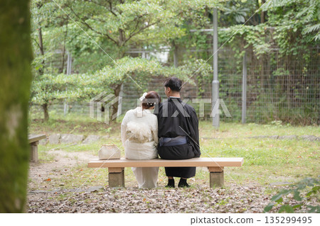A couple in kimonos sits on a bench in a lush park. Japan A couple in kimonos sits on a bench in a lush park. Japan 135299495