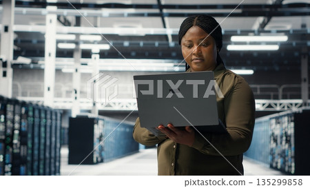 Data center workplace programmer using laptop to coordinate deployment of new server architecture. Server room worker using notebook to do rollout of cybersecurity framework, protecting data, camera B Data center workplace programmer using laptop to coordinate deployment of new server architecture. Server room worker using notebook to do rollout of cybersecurity framework, protecting data, camera B 135299858