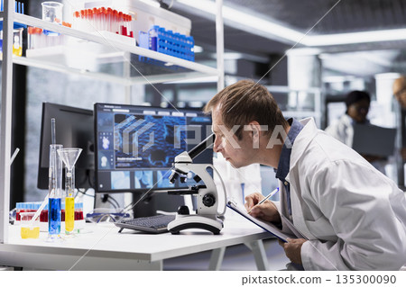 Scientist examines specimen under microscope with detailed focus in modern lab. Laboratory equipment and research study emphasize cellular observation and discovery in bioscience. 135300090