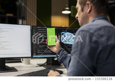 Green screen smartphone used by technician in startup office, optimizing code for performance and scalability. Mockup chroma key phone used by IT worker looking at programming language on PC Green screen smartphone used by technician in startup office, optimizing code for performance and scalability. Mockup chroma key phone used by IT worker looking at programming language on PC 135300116