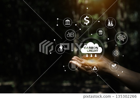 Hands holding a "CARBON CREDIT" cloud surrounded by a network of related icons, symbolizing the interconnected aspects of carbon trading and environmental sustainability. 135302266