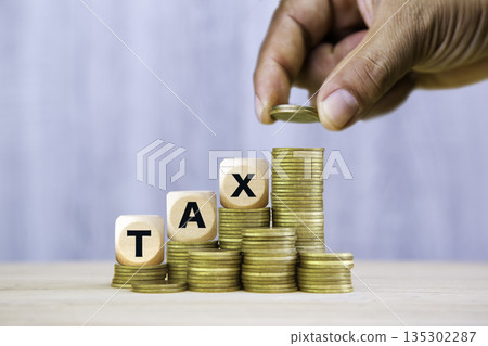 Hand placing a coin on stacks of coins with wooden blocks spelling TAX, symbolizing financial planning, government revenue, and the concept of taxation. Perfect for illustrating economic policies. 135302287