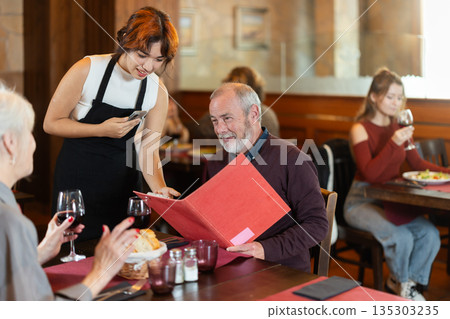 Young waitress taking order from elderly couple in restaurant 135303235
