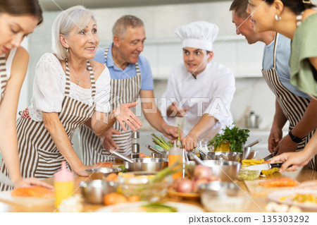 Positive attendees of cooking course talking cheerfully to each other in the kitchen Positive attendees of cooking course talking cheerfully to each other in the kitchen 135303292