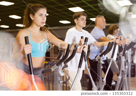 Young girl warming up on elliptical machine in gym Young girl warming up on elliptical machine in gym 135303312
