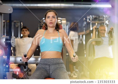 Portrait of young woman during workout with power exercise machine in gym 135303333