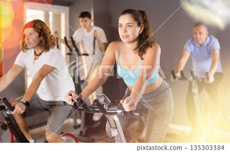 Man and woman taking indoor cycling class at fitness center, doing cardio riding bike Man and woman taking indoor cycling class at fitness center, doing cardio riding bike 135303384