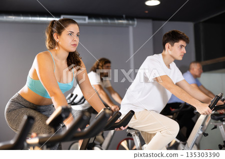 Young girl doing cardio workout on exercise bike in gym Young girl doing cardio workout on exercise bike in gym 135303390
