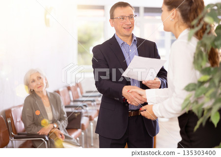 Middle-aged man handshaking with other person in waiting room Middle-aged man handshaking with other person in waiting room 135303400