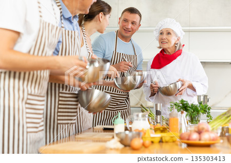 Elderly woman teaching cooking to group of people Elderly woman teaching cooking to group of people 135303413