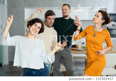 Friends dancing. Cheerful young people dancing and drinking while enjoying home party on room Friends dancing. Cheerful young people dancing and drinking while enjoying home party on room 135303457