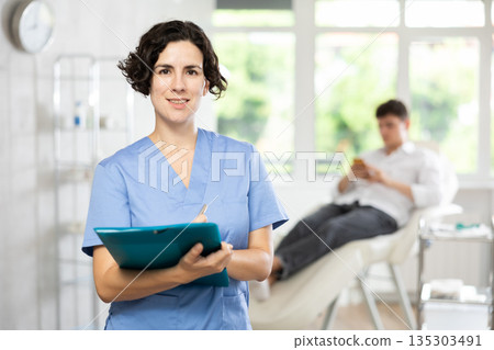 Middle-aged woman doctor posing in doctor's cabinet with document in hands Middle-aged woman doctor posing in doctor's cabinet with document in hands 135303491