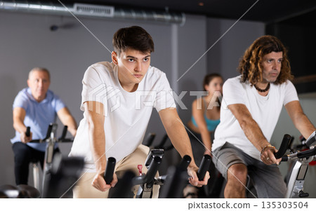 Man and woman taking indoor cycling class at fitness center, doing cardio riding bike 135303504