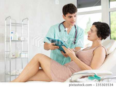 Middle-aged female patient signing papers while talking with man doctor 135303534