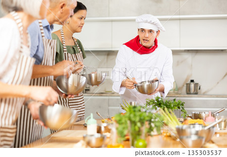Young guy cook teaches to cook group of people 135303537