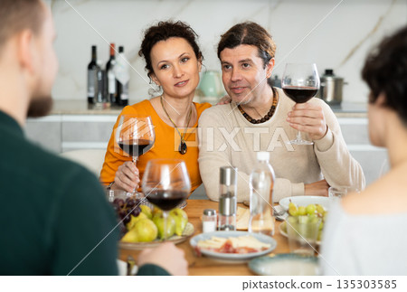 Two married couples are sitting at table, enjoying food and wine, chatting, talking, laughing. Two married couples are sitting at table, enjoying food and wine, chatting, talking, laughing. 135303585
